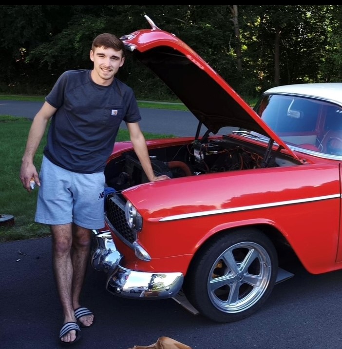 A picture of Aaron standing next to a red Cheverolet Bel Air.